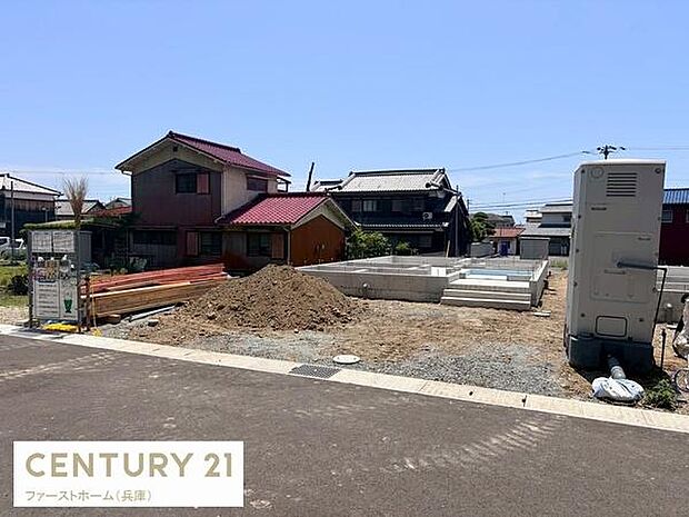 前面道路がしっかりと舗装されており現地の様子が分かりやすく撮影されています。周辺には落ち着いた住宅が立ち並び建築中の様子が確認できます。敷地の広がりやアクセスも視覚的に把握しやすい写真です。