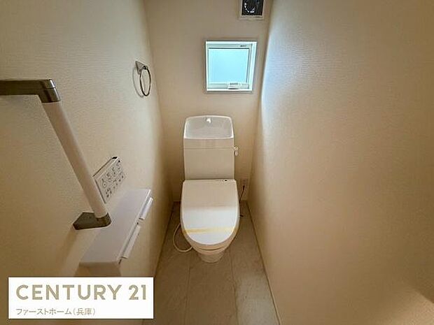 窓付きで換気しやすいトイレです。手すりが設置されており使いやすさにも配慮されています。ペーパーホルダーやリモコンが壁に設置されすっきりとした印象です。落ち着いた色合いでまとまった内装です。
