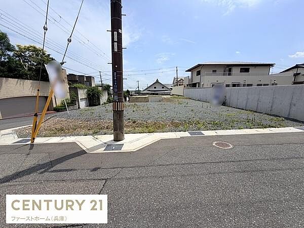 広々とした現地土地写真です。周囲は住宅が並び落ち着いた雰囲気が感じられます。前面道路が整備されており歩道も確保されています。柵や壁で囲まれているためプライバシー性も感じられます。