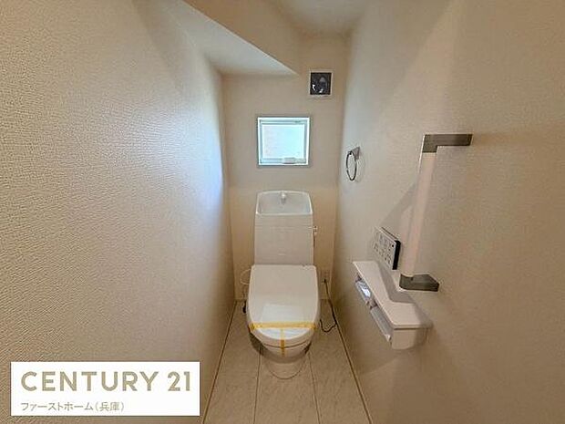 コンパクトで落ち着いた雰囲気のトイレです。手すりが設置されているため安心してご利用いただけます。小窓があり自然な明るさが感じられます。壁付けのペーパーホルダーや棚も設置されています。