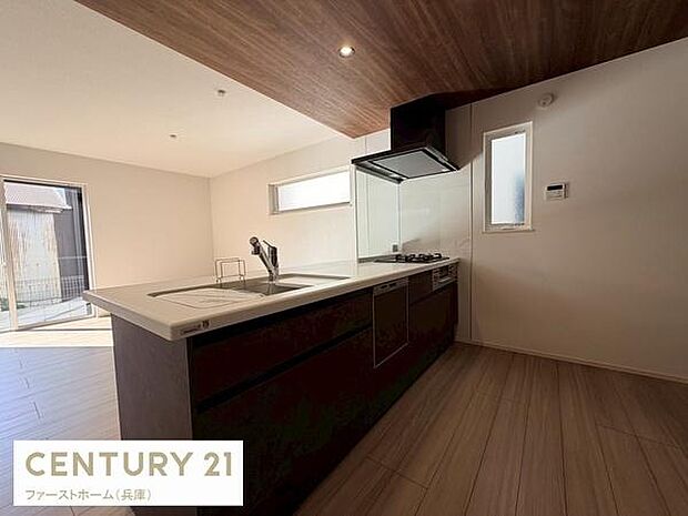 広々としたキッチンが空間に開放感を演出しています。明るい光が差し込む窓が特徴的です。シックなカラーのキッチンが洗練された雰囲気を感じさせます。床や天井の木目調デザインが落ち着きを加えています。