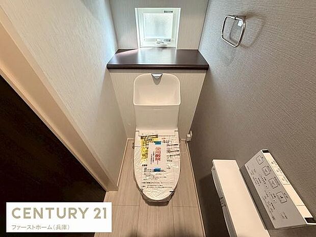 窓があり換気がしやすいトイレです。手洗い一体型のデザインで空間を有効に活用しています。ペーパーホルダーや棚も備わっています。落ち着いた色合いの内装です。