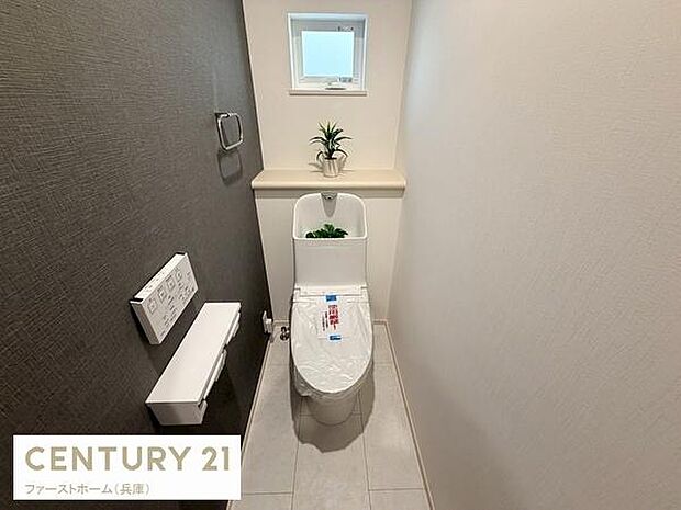 窓からの自然光が感じられるトイレです。落ち着いた色合いの内装で清潔感があります。使いやすいレイアウトと収納棚も備わっています。照明と床材にもこだわりが見られます。