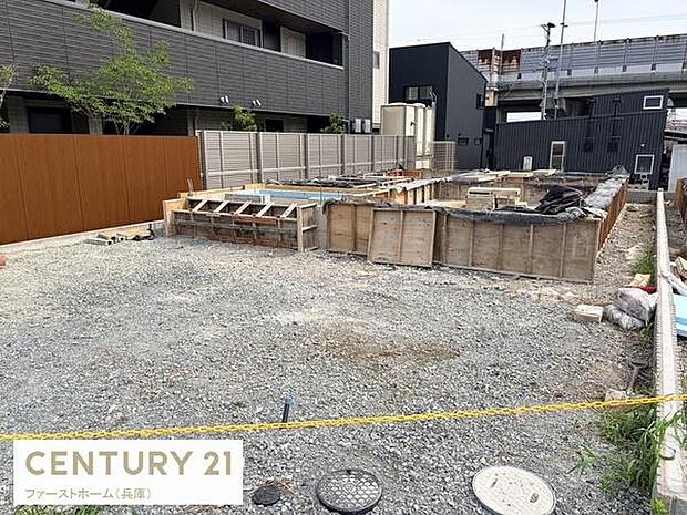 建築中の様子が確認できる現場写真です。敷地は広々としており資材の整頓も行き届いています。周囲は住宅やフェンスで囲まれており落ち着いた環境となっています。建物の基礎部分がしっかりと造られています。