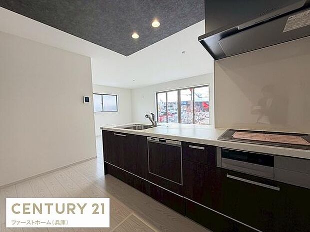 シックな色合いのキッチンが空間に落ち着きをもたらします。広い作業台で調理の効率も上がります。大きな窓から明るい光が差し込む開放的な雰囲気です。収納スペースも充実しています。