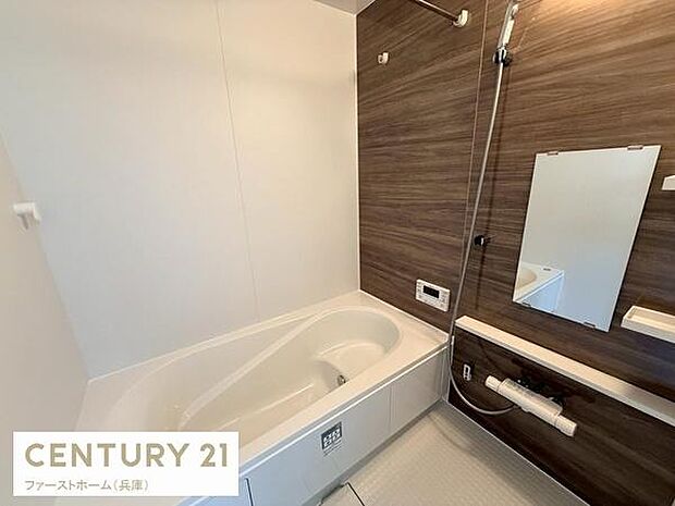 ナチュラルな木目調のアクセントパネルが特長的なバスルームです。壁付けのミラーや収納棚が配置されています。浴槽は広々とした造りです。シャワースペースもゆったりしています。