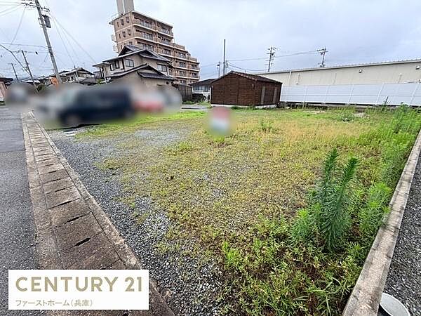 道路に面した現地土地写真です。平坦な地形で建物の建築に適しています。ゆとりある広さが特徴的です。周囲には住宅や施設があり生活利便性を実感できます。複数の用途に柔軟に対応できる土地です。