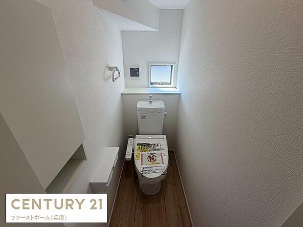 小窓が設けられており採光と換気に配慮されたトイレです。白を基調とした清潔感のある空間が広がっています。収納スペースも確保されており使い勝手に配慮されています。温水洗浄便座が設置されています。