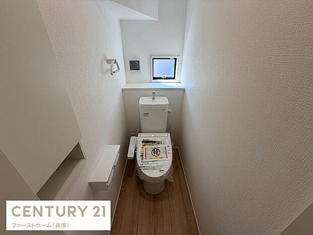 清潔感のあるシンプルなトイレ空間です。小窓からの明るい光が室内をすっきりと見せます。壁付け収納とペーパーホルダーが使い勝手に配慮されています。床の木目調が落ち着いた印象です。