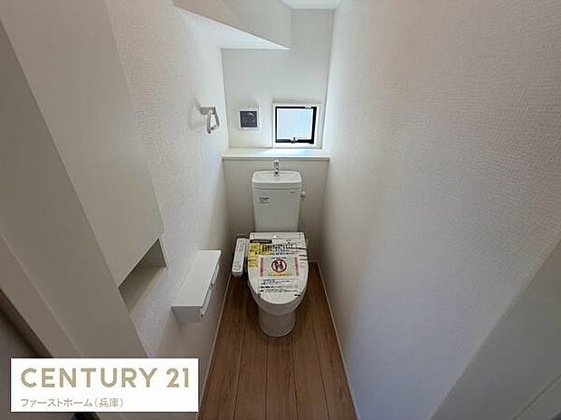 コンパクトな空間に機能的なトイレが設置されています。小窓があり換気に配慮されています。壁面には収納スペースも用意されています。清潔感のある内装が特徴です。