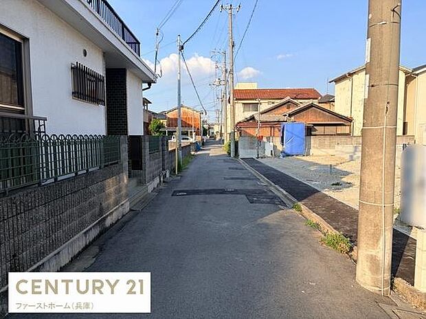 前面道路は舗装されており歩道と車道が明確に分かれています。周辺には住宅が並び落ち着いた雰囲気が広がっています。電柱や配線も整然と配置されており町並みがすっきりしています。