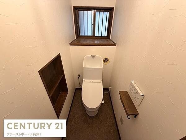 窓があり自然光が差し込む明るいトイレです。壁面に収納スペースが設けられており使い勝手も工夫されています。シンプルなデザインで清潔感が感じられる空間です。落ち着いた色合いが特徴的です。