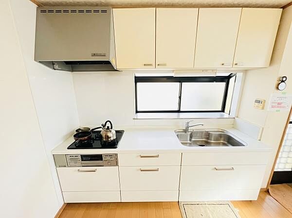 白を基調とした明るく清潔感のあるシステムキッチンです。調理スペース前の窓から自然光が入り、換気もスムーズに行えます。※AIによる画像加工を行っております。