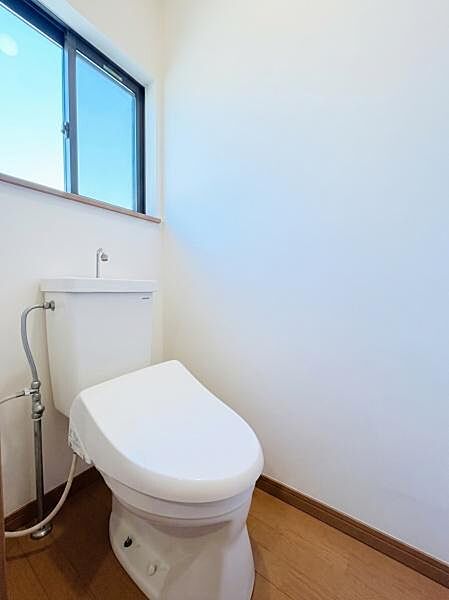 白を基調とした清潔感あふれるトイレ空間です。大きめの窓が設置されているため自然光が入り明るく、手軽に換気ができて衛生的です。※AIによる画像加工を行っております。