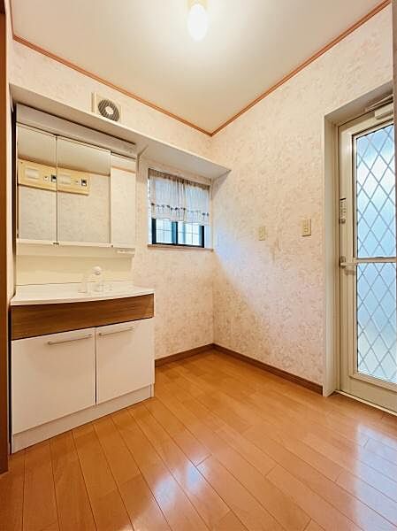 明るい木目調のフロアと上品なクロスが印象的な洗面脱衣所です。大きな三面鏡付き洗面化粧台を備え、小窓からの採光・通風も良好。※AIによる画像加工を行っております。