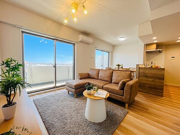 大きな窓から青空が広がる開放的なリビングです。木目調の床とブラウンのソファが温かみを演出し、明るくリラックスできる空間である点が最大の魅力です。