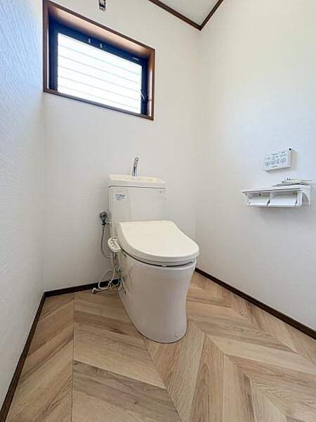明るい採光のあるトイレです。清潔感のある内装が特徴的です。ヘリンボーン柄の床が空間にアクセントを加えています。通風窓付きで使いやすい空間です。