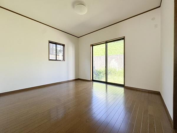 窓とガラスドアから自然光がしっかり入る洋室です。落ち着いた色合いのフローリングが特徴で使いやすい間取りです。シンプルなデザインなので家具の配置も調整しやすい空間です。