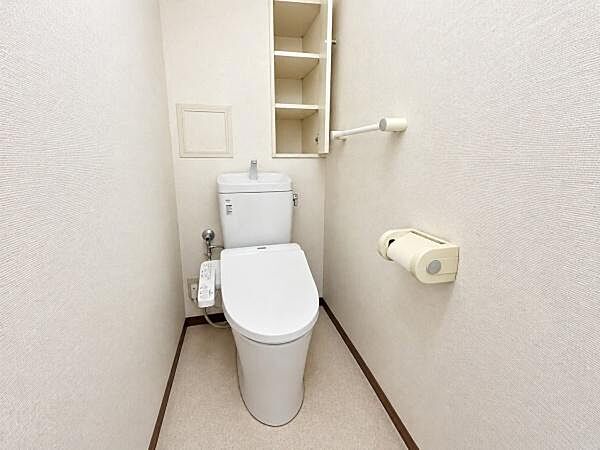 ウォシュレットトイレを備えた、白を基調とした空間です。壁面には吊戸棚があり、トイレットペーパーなどの収納に使えます。※現況写真から家具等を消去したAI加工イメージです