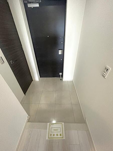 明るいホワイト系の壁面と高級感のある床タイル、シックな扉が美しく調和した玄関ホールです。落ち着いた質感のタイル敷きとなっております。