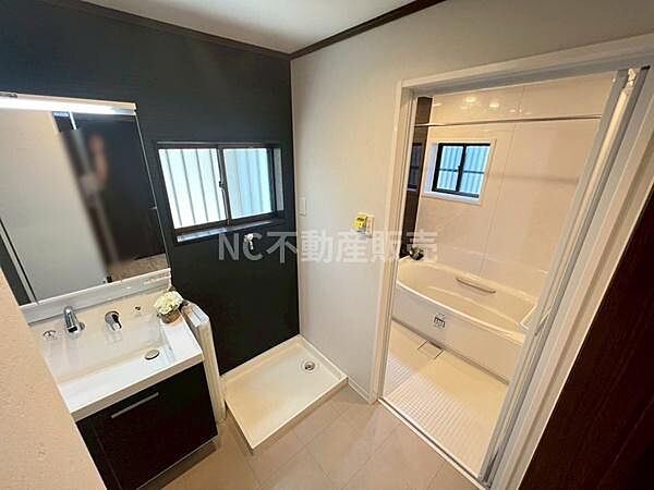 洗面台と浴室が隣接し使い勝手の良い動線です。窓があり明るい空間になっています。洗面スペースに収納も備わっています。ダークカラーのアクセント壁が洗練された印象を与えます。清潔感のある洗面所です。