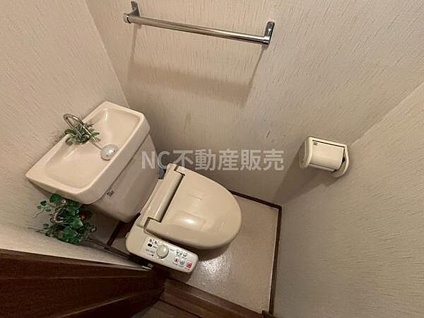 温水洗浄便座が備え付けられているトイレです。タオル掛けやペーパーホルダーも設置されています。手洗い器付きで使い勝手の良い空間です。清潔感のある内装も特徴です。コンパクトにまとまった設計となっています。