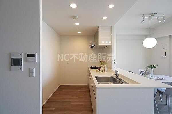 明るい照明が印象的なキッチンです。カウンター越しにリビングダイニングが見渡せます。フラットな作業スペースが確保されています。床は木目調で落ち着いた雰囲気を感じます。シンプルなデザインが魅力です。