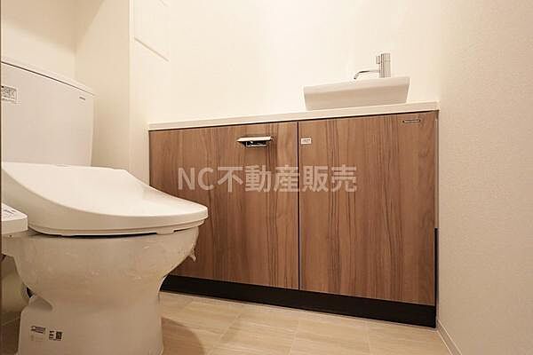 シンプルな内装で使いやすいトイレです。木目調の収納が空間に温かみをプラスしています。独立型の手洗い器が設置されており実用的な設備です。清潔感のあるフロアでお手入れもしやすい印象です。
