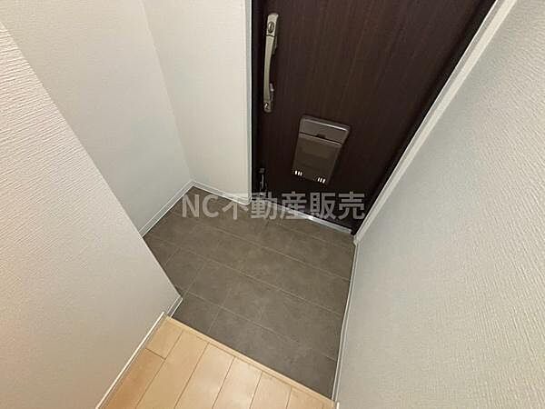 玄関はシンプルなデザインで明るい色合いの壁が空間を広く感じさせます。ダークカラーのドアが全体を引き締め落ち着いた雰囲気を演出しています。床は汚れが目立ちにくい素材で使いやすさも考慮されています。