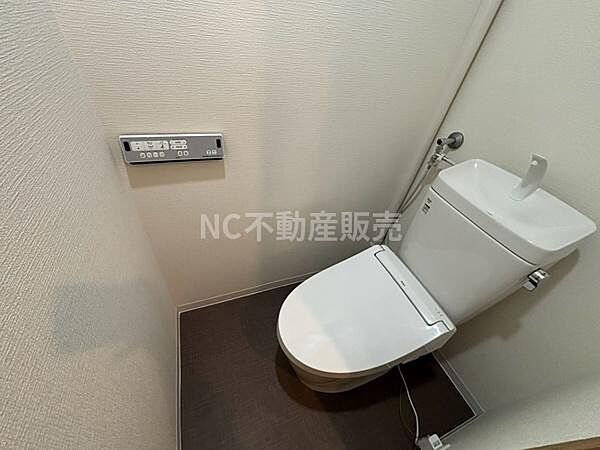 シンプルなデザインのトイレで清潔感のある空間です。壁面に操作パネルが設置されており使いやすさが考慮されています。手洗い付きのタンクが実用的です。床の色合いが落ち着いた印象を与えます。