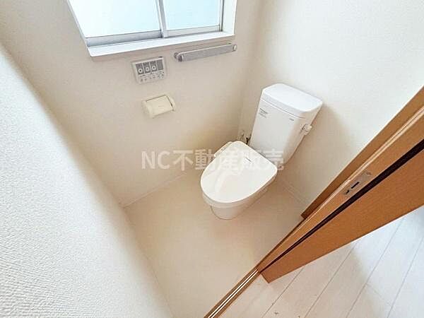 清潔感のあるトイレ空間です。窓が設置されており換気しやすい造りになっています。シンプルで使い勝手の良いデザインです。ペーパーホルダーや操作パネルも設けられています。