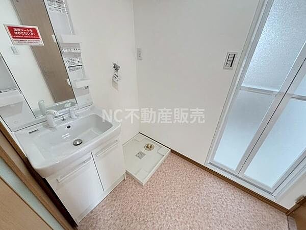 シンプルで清潔感のある洗面台が設置されています。鏡の収納スペースが充実しており小物の整理に便利です。隣には洗濯機置場も確保されています。洗面所には窓があり明るい空間となっています。