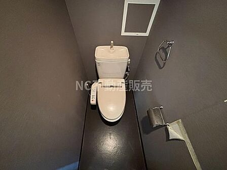 シンプルで落ち着いた色合いのトイレ空間です。ウォシュレット機能が備わっており使い勝手に配慮されています。壁面には収納や小物掛けも設置されています。手元で操作できる設備が揃っています。