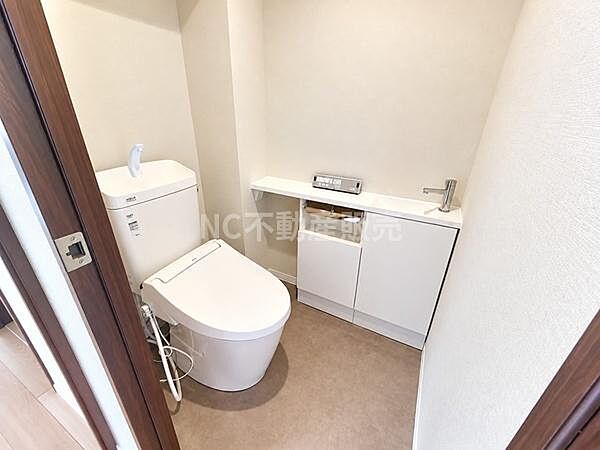 清潔感のあるトイレ空間です。収納スペースも確保されており使い勝手の良いレイアウトになっています。手洗い場付きで利便性が高い点も魅力です。落ち着いた色合いの内装が印象的です。