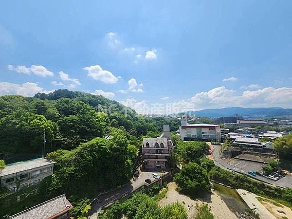 現地からの眺望を一望できる写真です。緑豊かな自然が広がり空の広がりも感じられます。周辺には川や建物が点在しており遠くの山並みまで見渡せます。晴れた日の景色が印象的です。