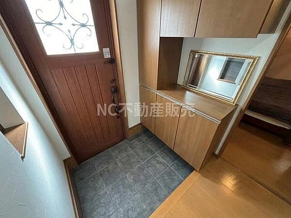 玄関には収納が充実しており整理整頓がしやすい空間です。落ち着いた色合いの木製ドアがアクセントになっています。大きな鏡が設置され外出前の身だしなみ確認に便利です。床はタイル仕様で手入れが簡単です。