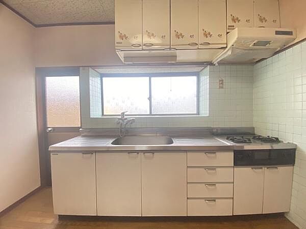 窓から自然光がしっかり差し込む明るいキッチンです。落ち着いたトーンのタイルが清潔な印象を与えます。豊富な収納スペースがあり使い勝手の良いシンクとコンロの配置です。