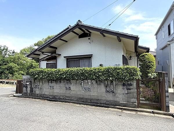 切妻屋根の美しいシルエットが際立ち、緑豊かな生垣と装飾門扉が落ち着いた住環境を感じさせます。