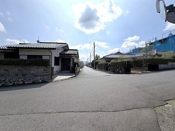 接道する道路の全景。見通しが良く、周辺も同規模の戸建が並ぶ落ち着いた住環境です。土地正面のアプローチ部分も確認いただけます。