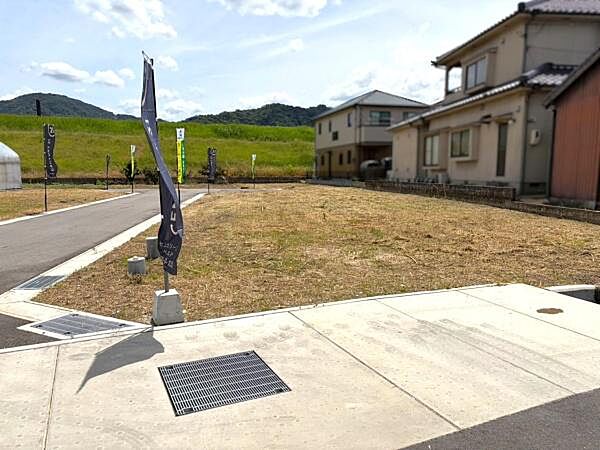 現地写真よりすぐ近くに舗装された前面道路があり周辺は落ち着いた住環境が感じられます。周囲には住宅が建ち並び開放感があります。