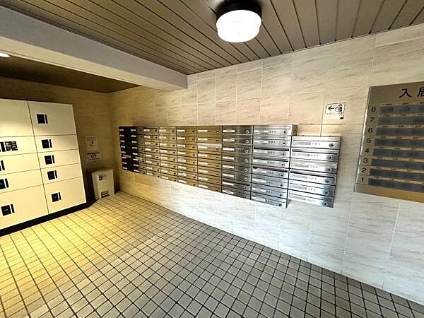 明るい照明が印象的なエントランスです。複数の郵便受けが設置されており整理された空間となっています。宅配ボックスも完備され利便性が高いです。タイル床が落ち着いた雰囲気を演出しています。