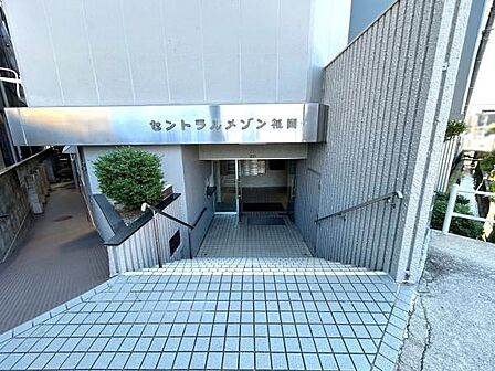 エントランスは広々としたタイル敷きで開放感があります。階段には手すりが設けられており安心してご利用いただけます。入口付近にはグリーンが配置され落ち着いた印象です。