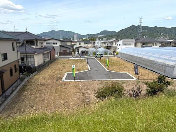道路に面した現地土地写真です。周囲には住宅が立ち並び落ち着いた印象の街並みです。敷地は整形地で活用しやすそうな形状です。区画ごとに分かれており車の出入りもスムーズに感じられます。