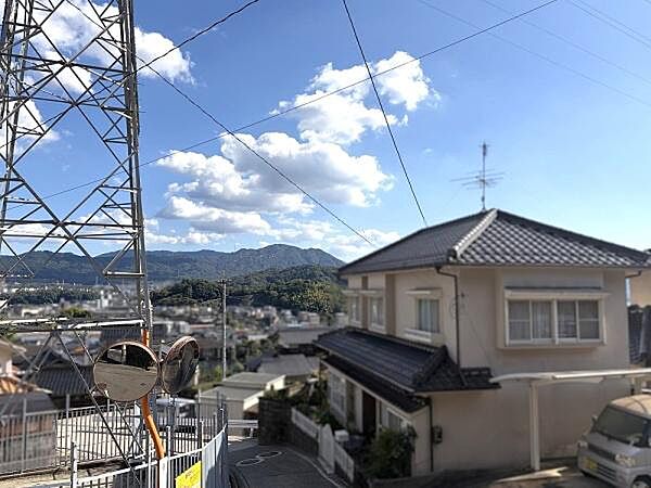 遠くに広がる山々を望める眺望が楽しめます。青空と白い雲が清々しい印象を与えます。周辺の住宅街も見渡せる開放感のある現地からの景色です。町全体の雰囲気を感じられます。