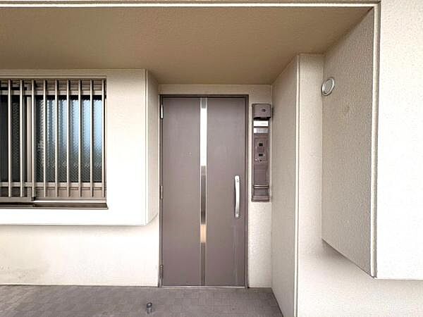 玄関ドアはシンプルなデザインで周囲の外観と調和しています。インターホンが設置されており来客時の対応も安心です。窓には格子があり防犯面にも配慮されています。すっきりとした印象の玄関です。