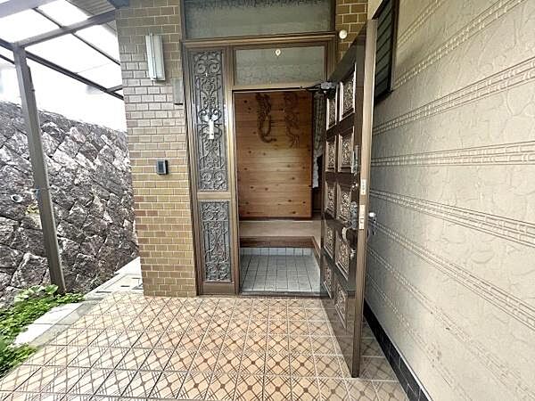 屋根付きのポーチは雨の日の出入りにも配慮された実用的な設計。玄関扉は花柄のレリーフが施された重厚な彫刻扉。上部と側面に採光ガラスがあり、扉を閉めていても玄関ホール内に自然光が差し込む明るい空間を実現。