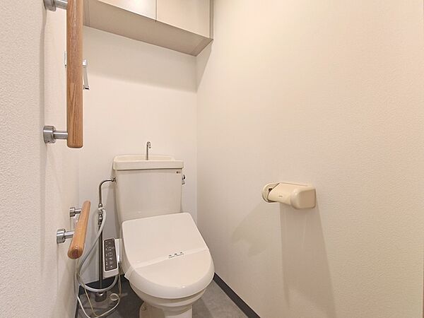 手すりが配されたトイレ。 吊戸棚収納も配備され、不便のない空間となっております。