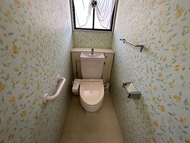 【トイレ】黄色い花柄の壁紙が、明るい印象のトイレ。快適にご使用いただける、温水洗浄便座付きです。手すりがあり、立ち上がりの際の転倒を予防してくれます。