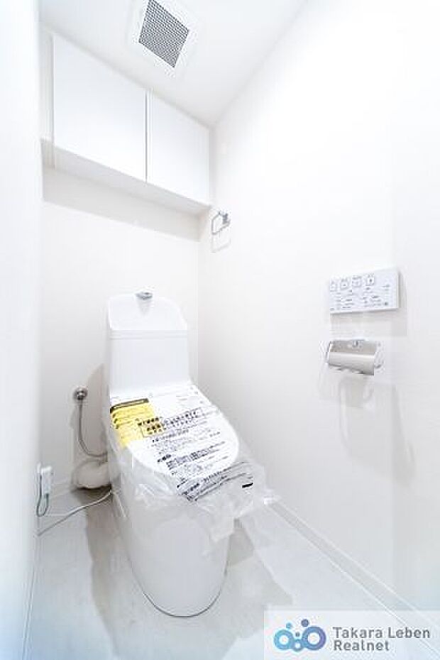 白を基調に清潔感のあるトイレ。トイレットペーパーホルダーとタオル掛けは標準で実装してます。上部に吊戸棚があり、掃除用具などの収納場所に困りません。