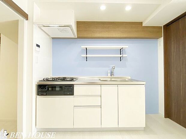 キッチン・爽やかなブルーのアクセントクロスを施したキッチンスペースです。壁面に棚があり、スパイスなどをスッキリ収納できます。